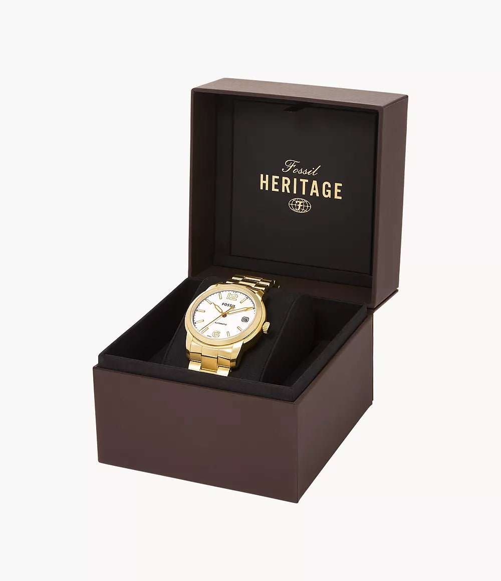 Reloj Fossil Heritage dorado presentado en caja original marrón, tapa abierta mostrando logotipo Heritage en el interior.