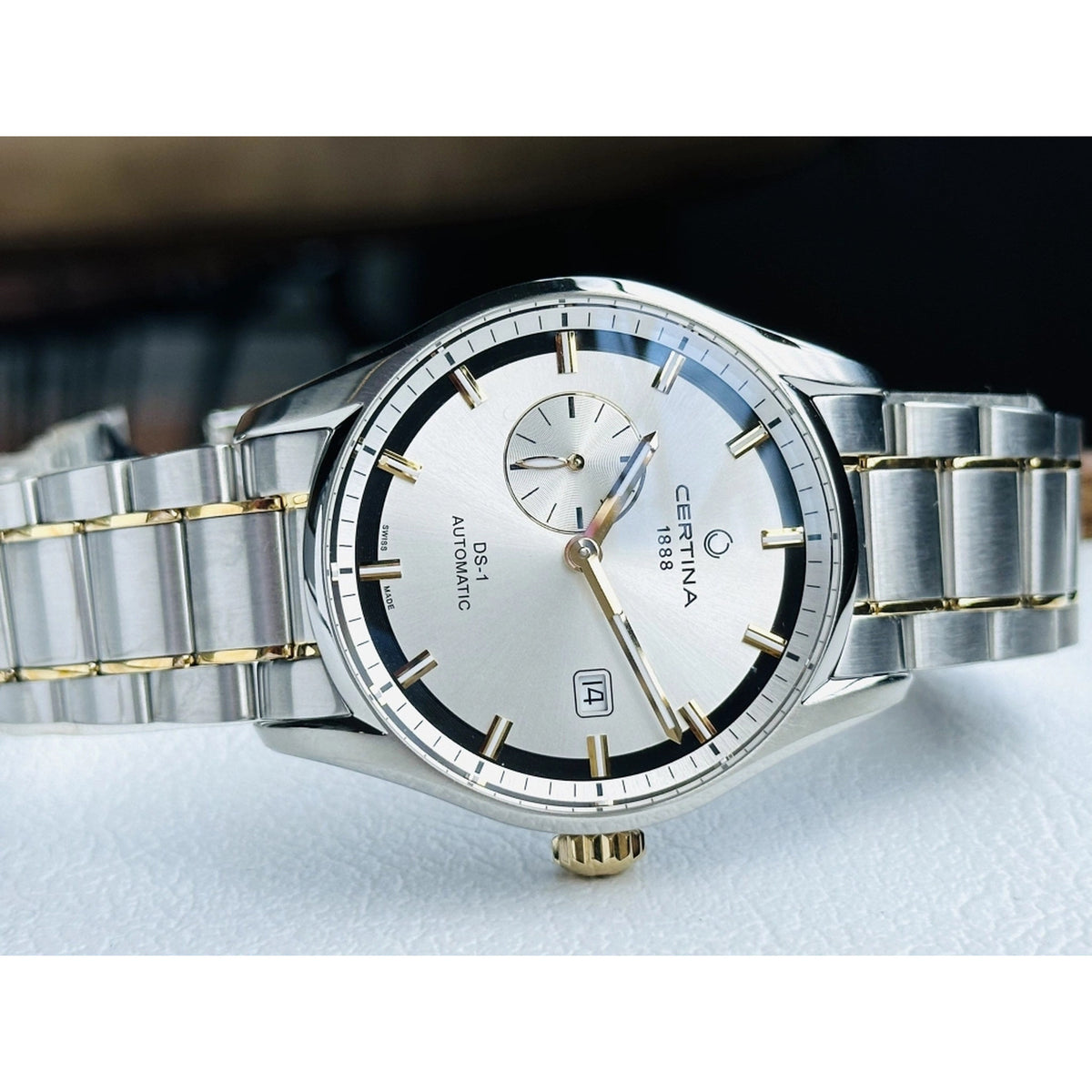 Certina DS-1 automatic men's watch angled to highlight the silver sunburst dial, gold-tone hands, small seconds subdial, and date window.