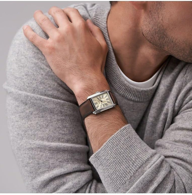 Hombre con jersey gris mostrando en la muñeca un reloj Fossil rectangular con esfera crema y correa de piel marrón.