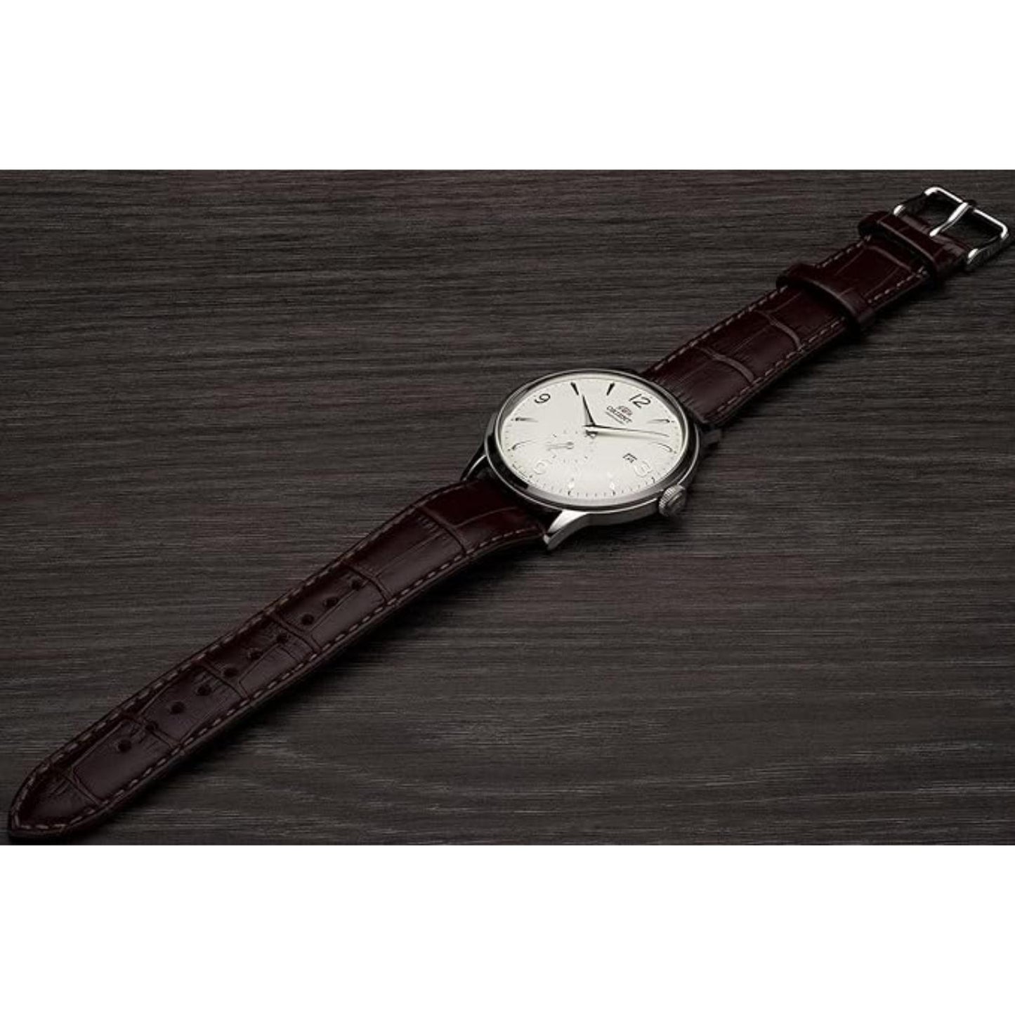 Orient Bambino Small Seconds RA-AP0002S10B automatic dress watch with white dial and brown crocodile-pattern leather strap displayed on a dark wooden surface.