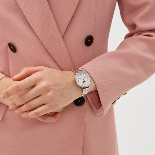 Reloj Fossil Jacqueline ES5164 sun moon de acero, puesto en muñeca de mujer con blazer rosa, esfera blanca y bisel cristal.