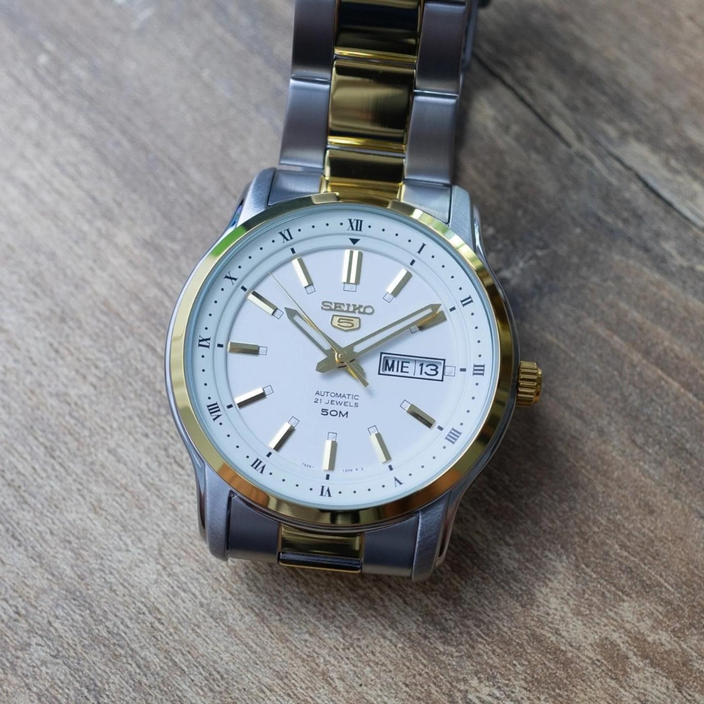 Seiko 5 SNKP14K1 automatic dress watch with white dial, gold-tone accents, day-date display and two-tone stainless steel bracelet in lifestyle setting.