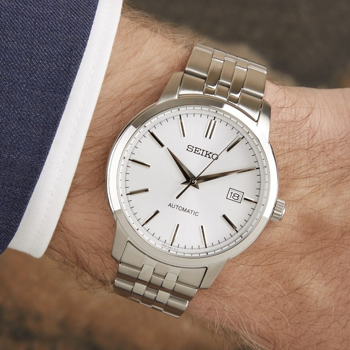 Close-up of the Seiko Essentials SRPH85K1 men's watch with silver dial and stainless steel link bracelet on wrist