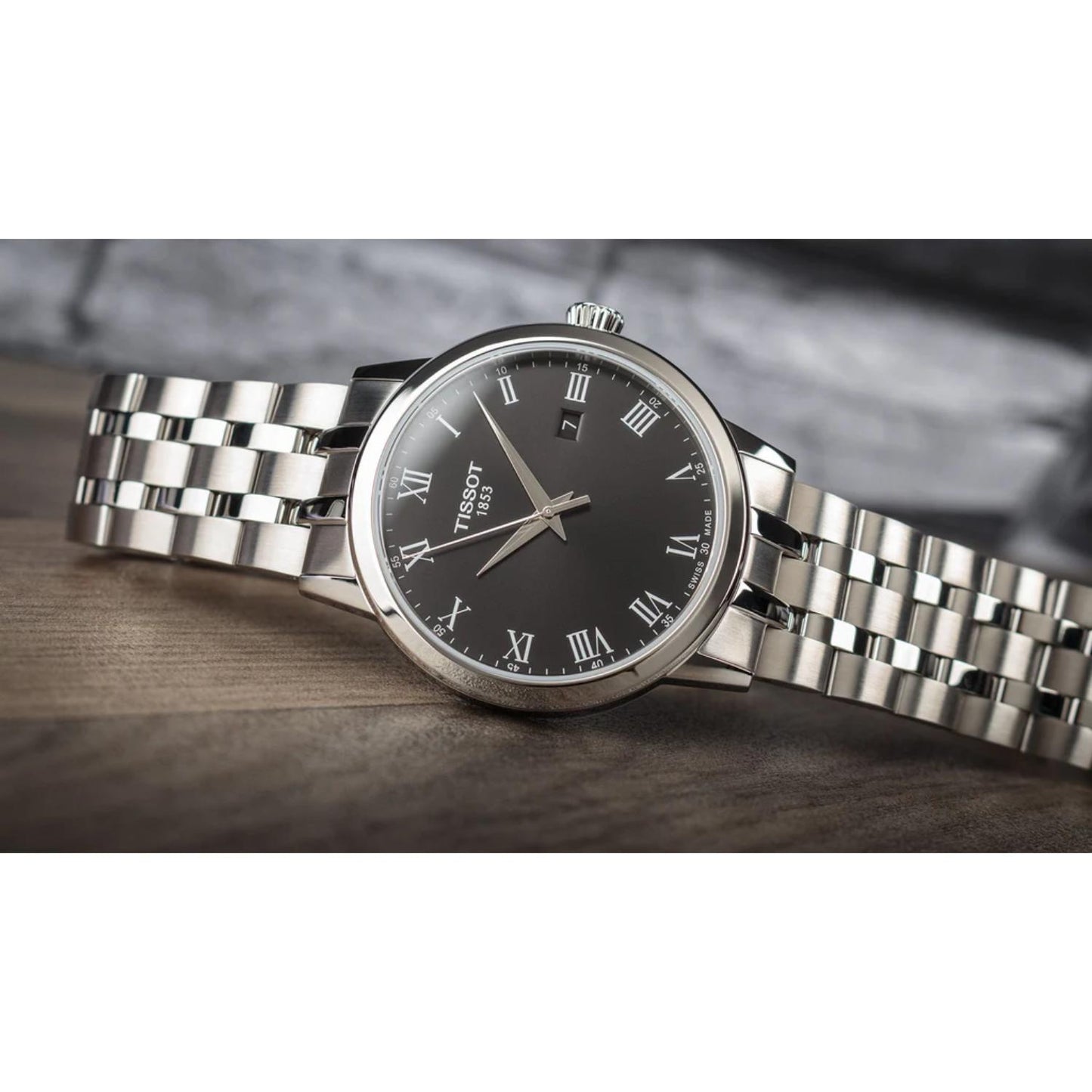 Reloj Tissot Classic Dream T129.410.11.053.00 apoyado en una superficie de madera, mostrando su esfera negra con números romanos y brazalete de acero pulido en un entorno de estilo elegante.