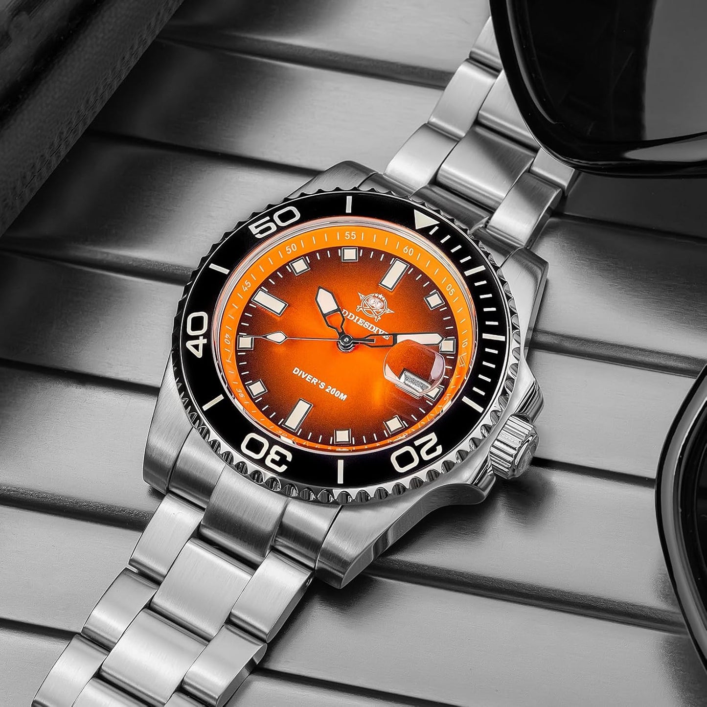 Reloj Addiesdive automático con esfera naranja visto en perspectiva superior, mostrando el brazalete de acero inoxidable y el bisel negro sobre una superficie metálica.