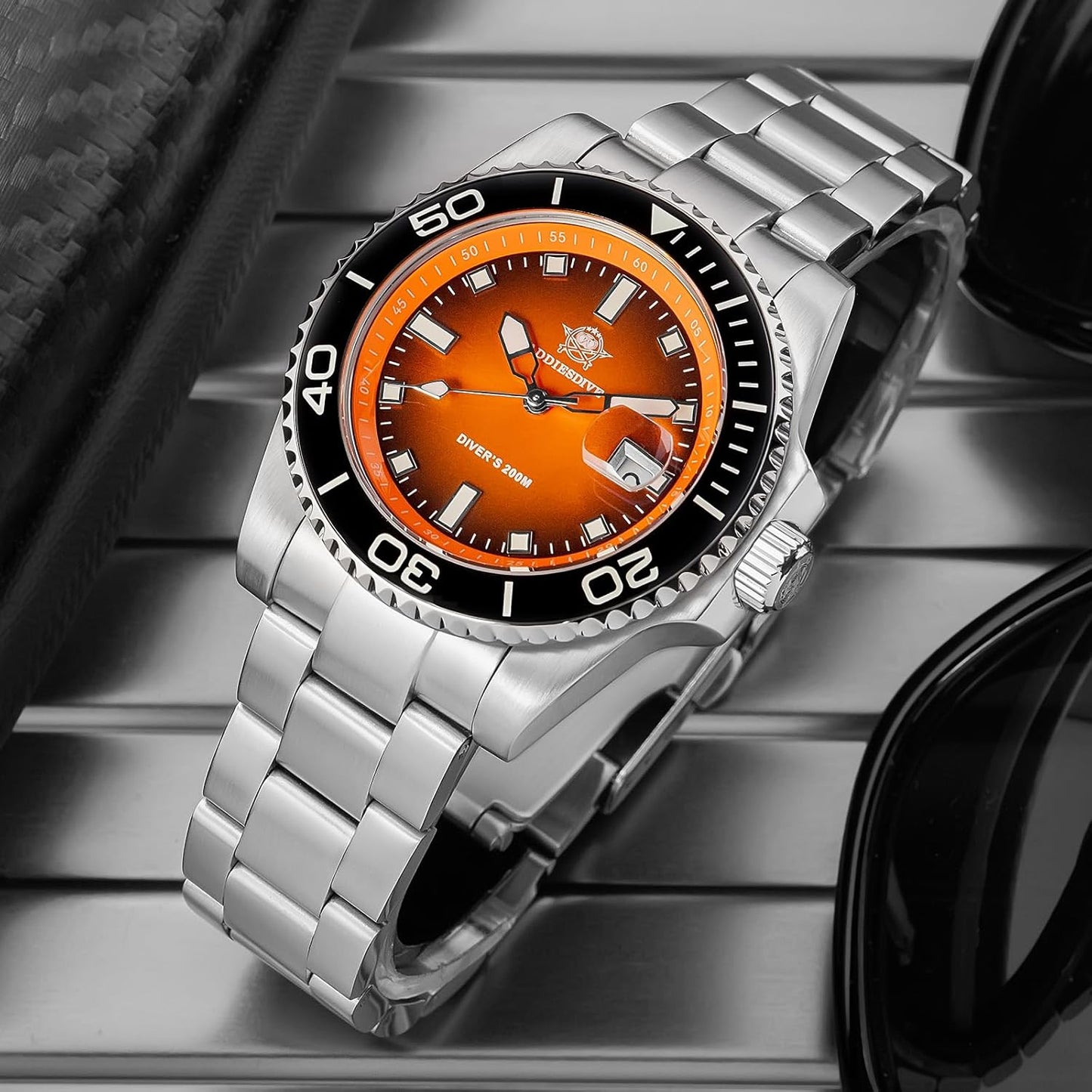 Reloj Addiesdive automático con esfera naranja visto en perspectiva, mostrando el brazalete de acero y el bisel negro sobre una superficie metálica.