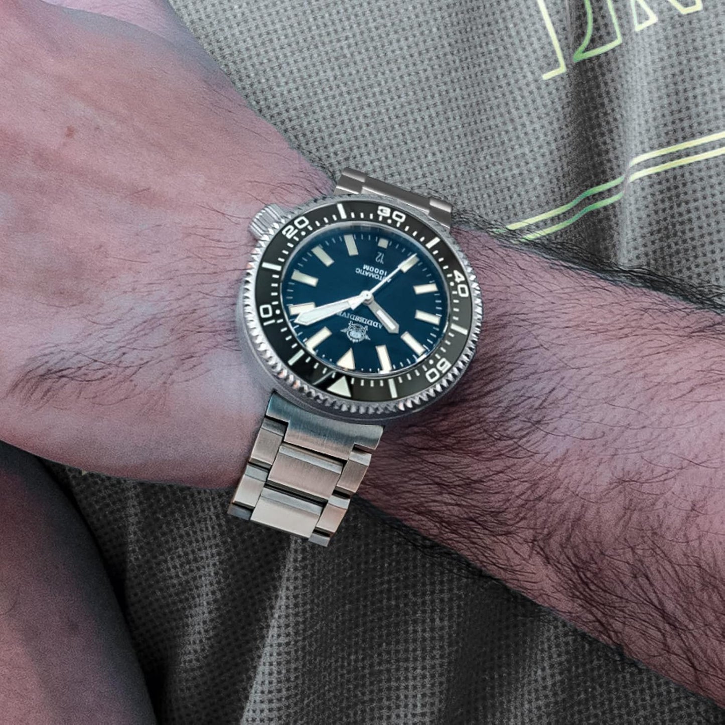 Reloj Addiesdive automático de acero con esfera negra lucido en la muñeca de una persona sobre camiseta deportiva.