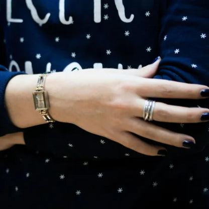 Reloj Anne Klein 10/4899SVTT en muñeca de mujer, caja rectangular bicolor y brazalete fino combinado con jersey azul marino