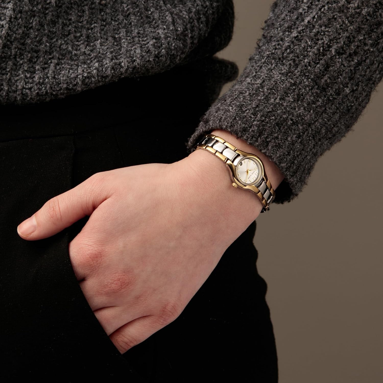 Reloj Anne Klein 10/6777SVTT en muñeca de mujer, brazalete bicolor oro y plata visible junto a jersey gris y pantalón negro