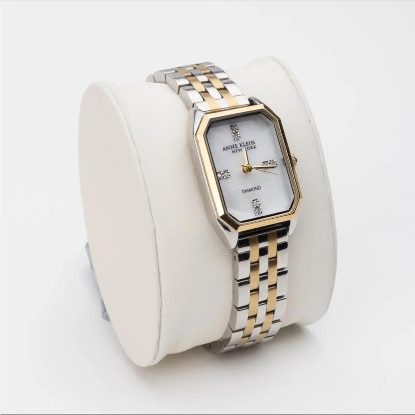 Anne Klein 12/7751MPTT with white mother-of-pearl dial, diamond accent markers, gold-tone bezel details, and two-tone bracelet displayed on a presentation cushion.