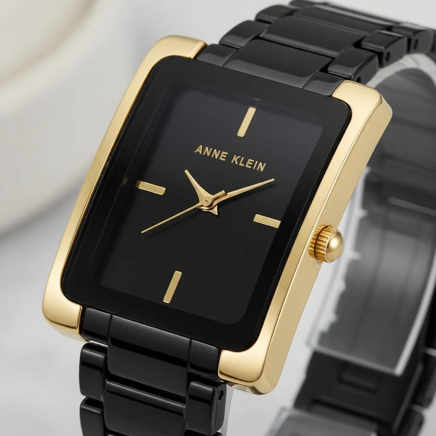 reloj Anne Klein AK/2952BKGB con caja rectangular dorada y esfera negra, mostrado en primer plano con corona lateral visible