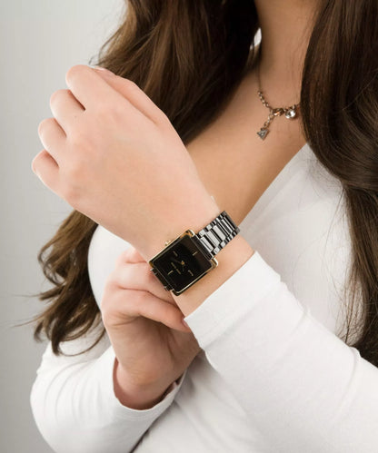 reloj Anne Klein AK/2952BKGB con caja rectangular dorada y esfera negra llevado en la muñeca con brazalete metálico negro