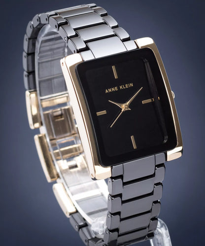 reloj Anne Klein AK/2952BKGB con esfera negra y caja rectangular dorada montado en brazalete metálico oscuro, mostrado en vista frontal ligeramente inclinada