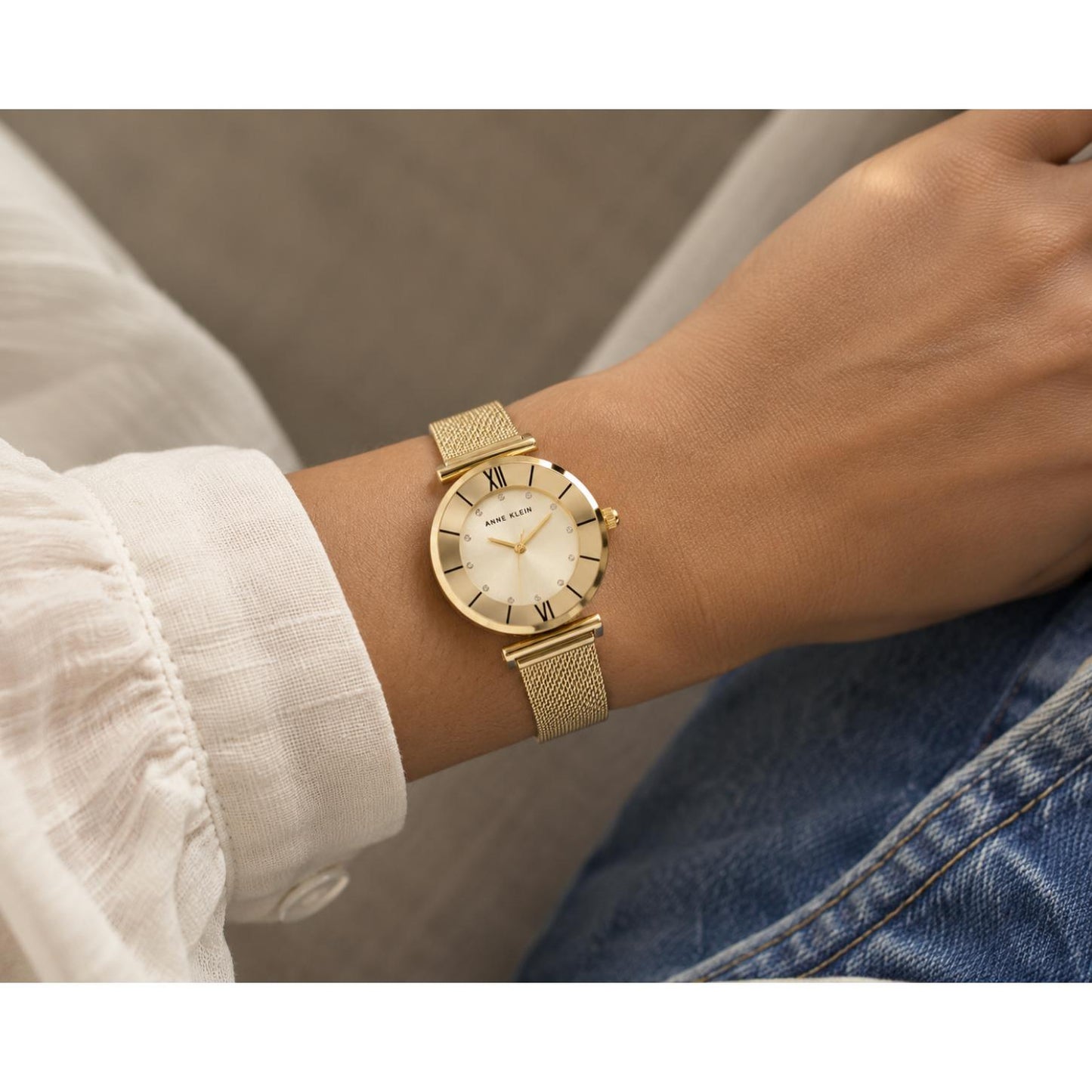 Anne Klein AK-3780CHGBST worn on the wrist with round dial, gold-tone case, Roman numeral markers, crystal accents, side crown, and gold-tone mesh bracelet.