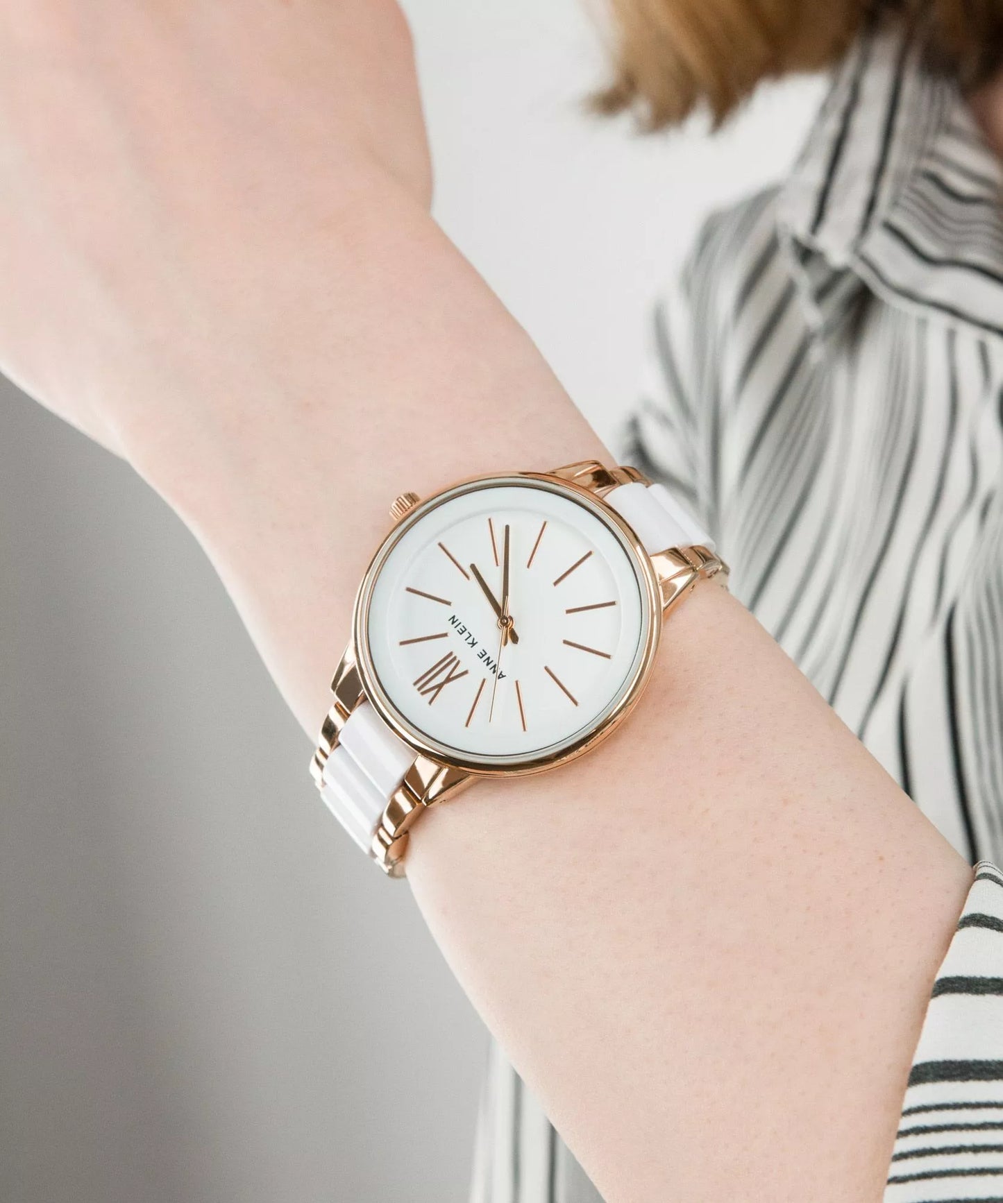 Reloj Anne Klein AK/1412WTRG en muñeca de mujer, brazalete blanco y oro rosa combinado con camisa de rayas