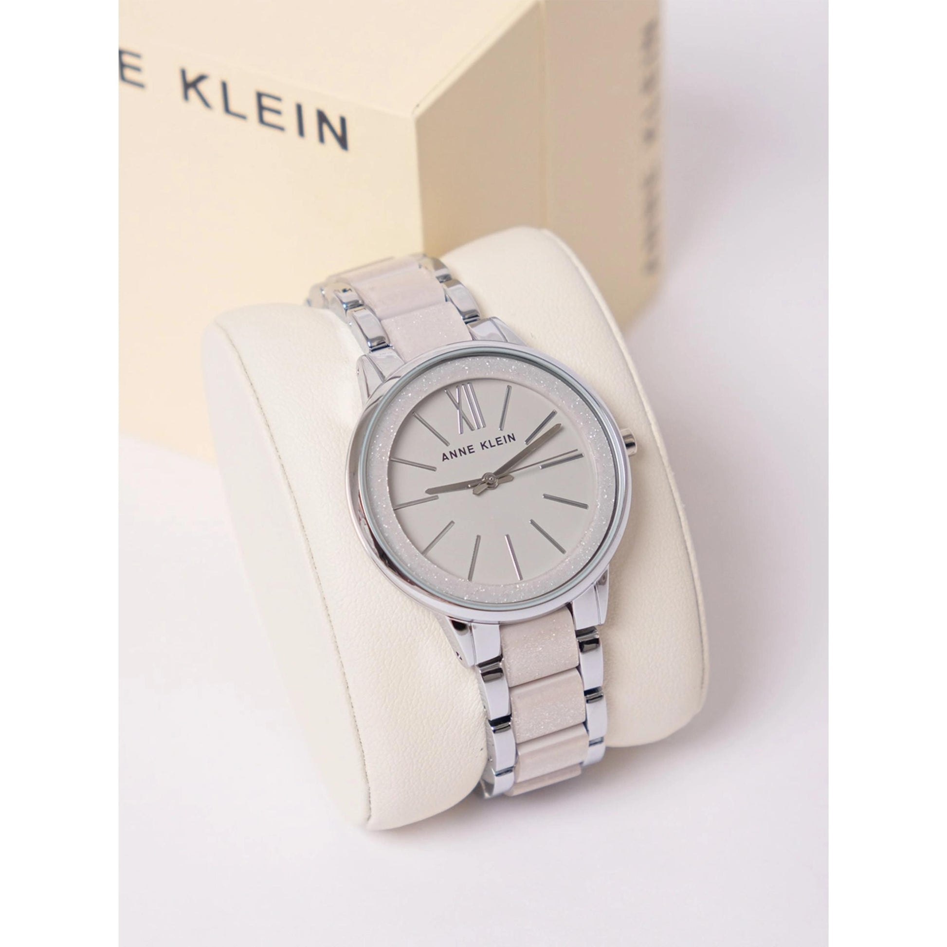 Anne Klein AK/1413LGSV with grey sunray dial, glitter bezel detail, and metallic silver bracelet displayed on a presentation cushion.