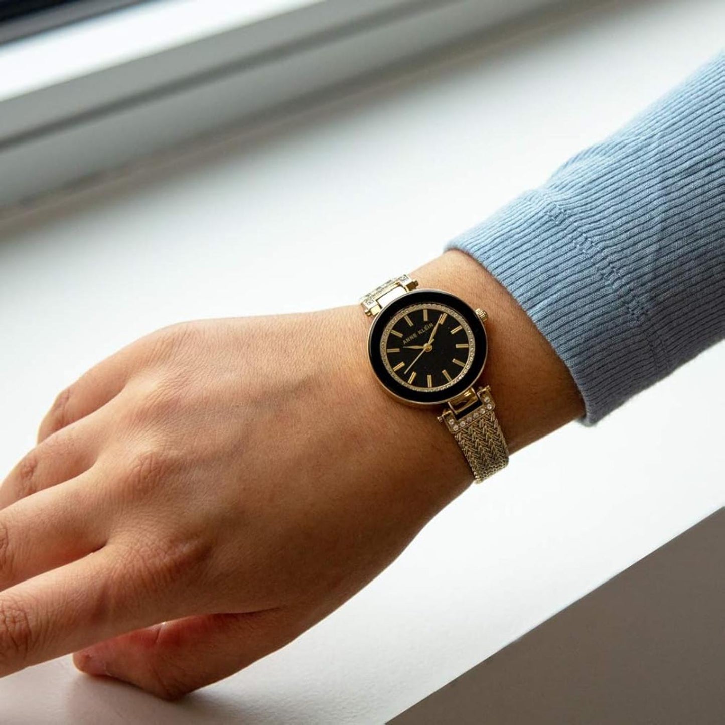 Anne Klein AK/1906BKGB with black dial, crystal-accented bezel, and gold-tone mesh bracelet worn on the wrist in an elegant everyday style.