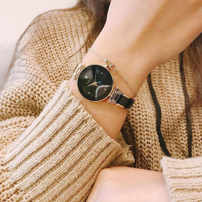 Reloj Anne Klein AK/1980BKGB en muñeca de mujer, esfera negra con diamante y brazalete negro combinado con jersey beige