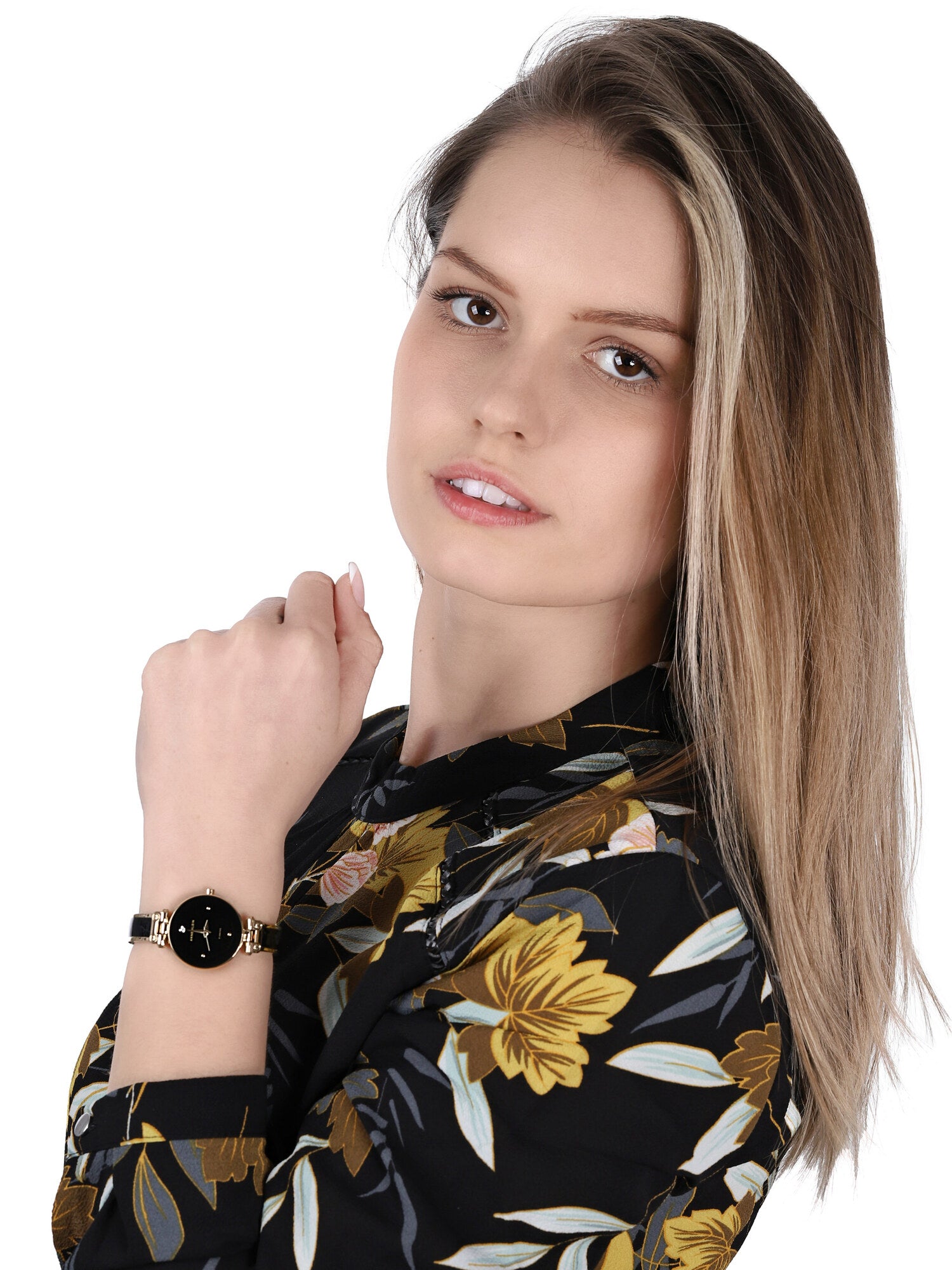 Reloj Anne Klein AK/1980BKGB en muñeca de mujer, esfera negra y brazalete dorado combinados con blusa floral oscura.