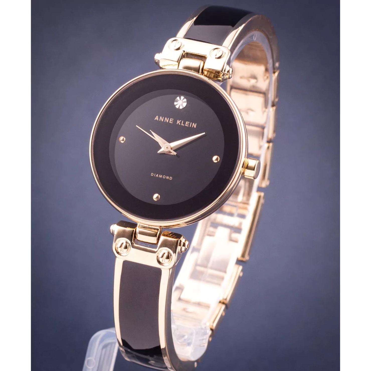 Vista lateral del reloj Anne Klein AK/1980BKGB, esfera negra con diamante y brazalete negro y dorado en soporte