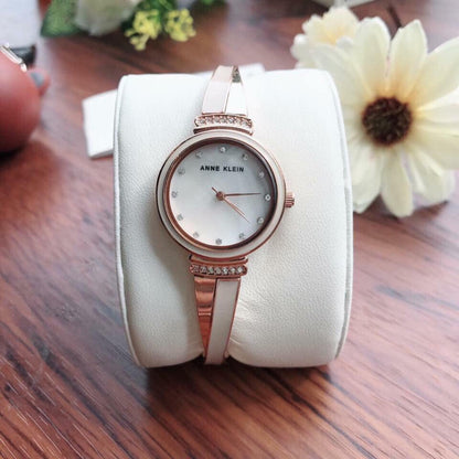 Anne Klein AK/2216BLRG with white mother-of-pearl dial, crystal hour markers, and rose gold-tone bangle bracelet displayed on a presentation cushion.