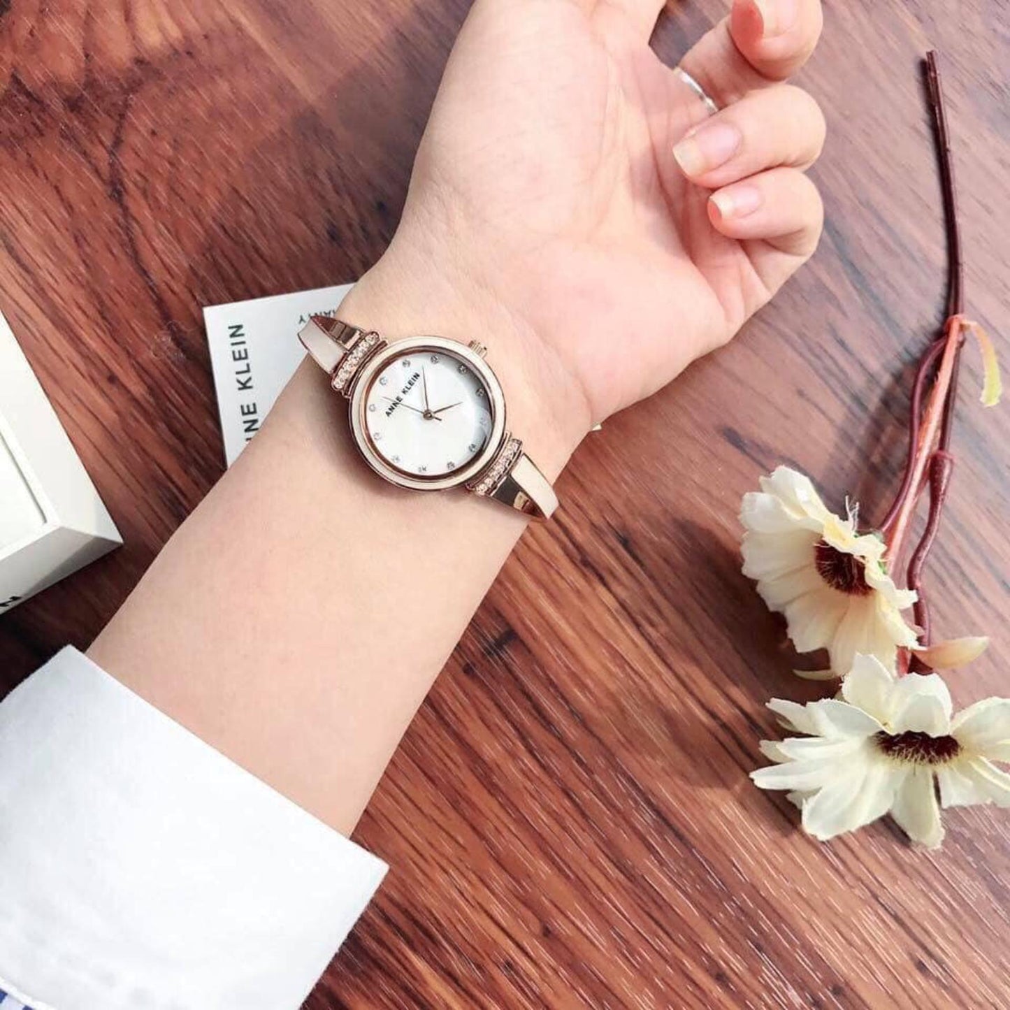 Anne Klein AK/2216BLRG with white mother-of-pearl dial, crystal hour markers, and rose gold-tone bangle bracelet worn on the wrist.