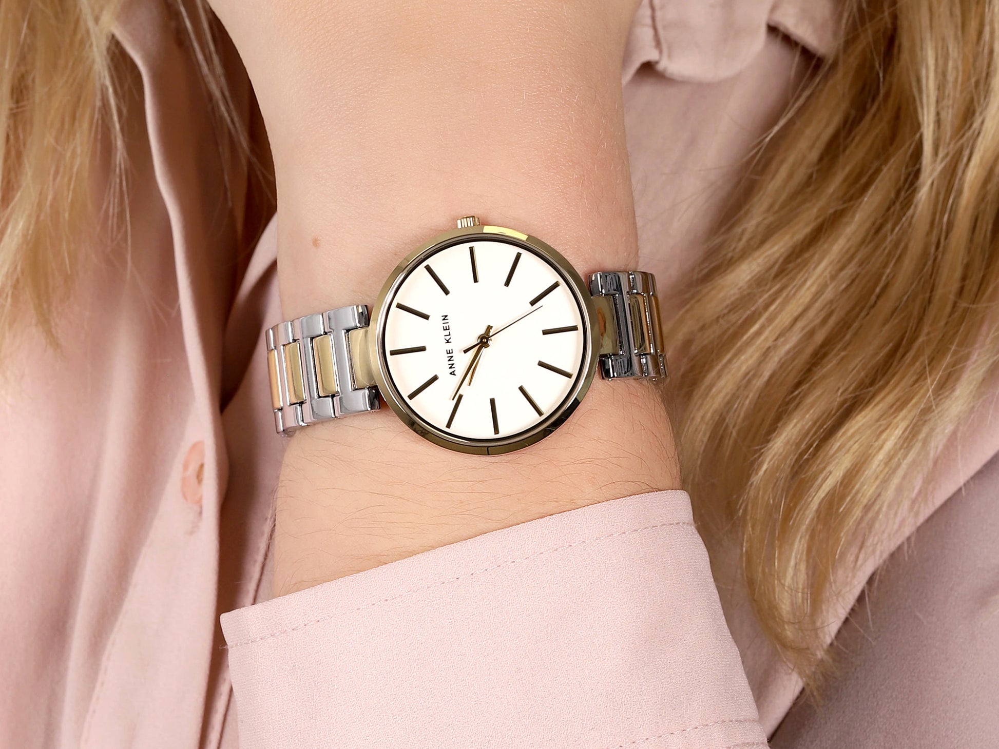 Reloj Anne Klein AK/2787SVTT en muñeca de mujer, esfera blanca y brazalete bicolor plata y dorado combinado con blusa rosa