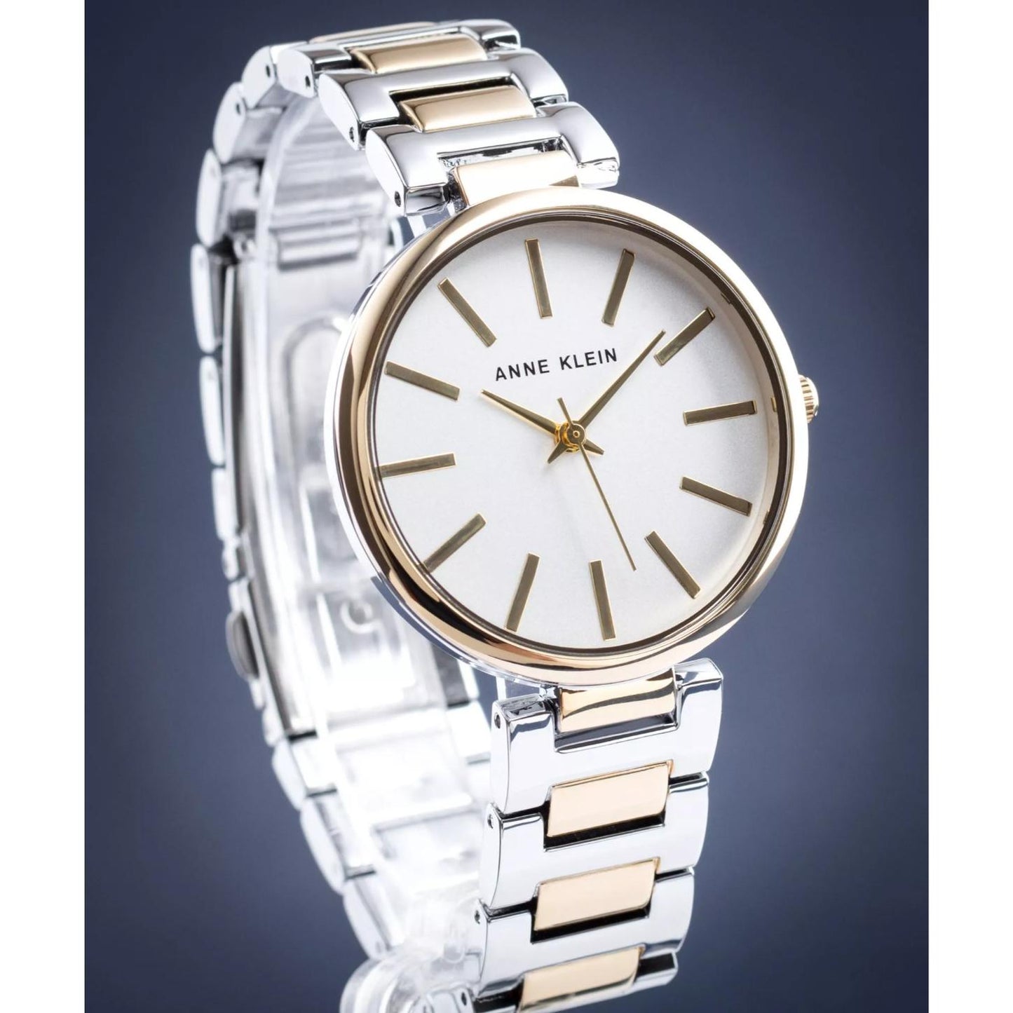 Reloj Anne Klein AK/2787SVTT en vista tres cuartos, esfera blanca y brazalete bicolor plata y dorado sobre fondo gris.