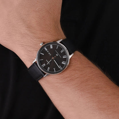 Reloj Bering para hombre con esfera negra, números romanos y correa de piel negra, visto en la muñeca.