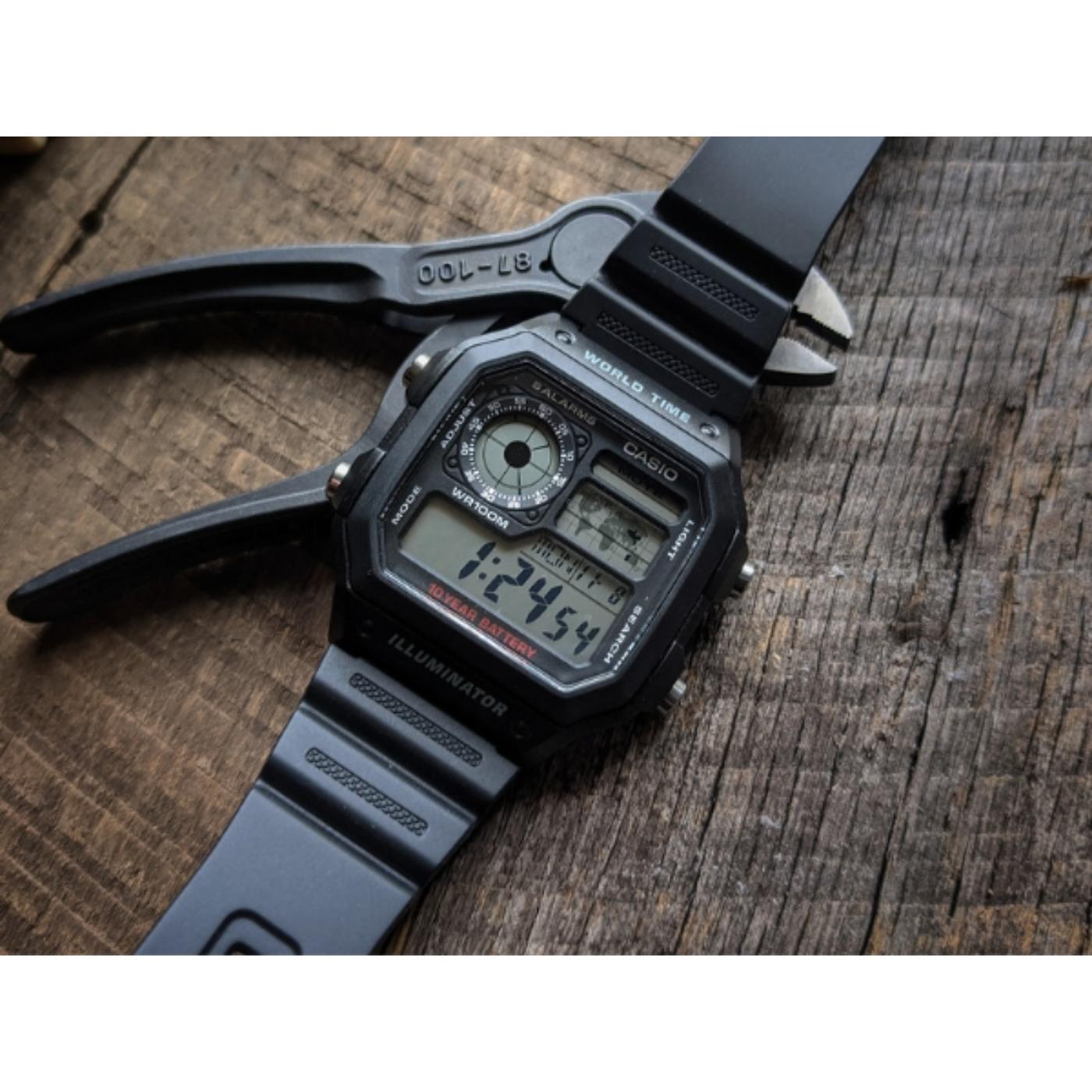 Casio AE-1200WH-1A digital watch with black resin strap being adjusted using a tool showing durable case and world time display