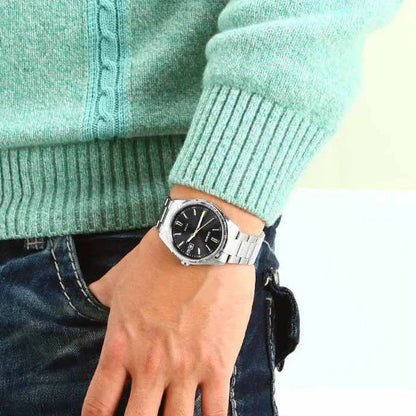 Reloj Casio analógico de acero con esfera negra lucido en la muñeca de una persona con jersey verde claro.