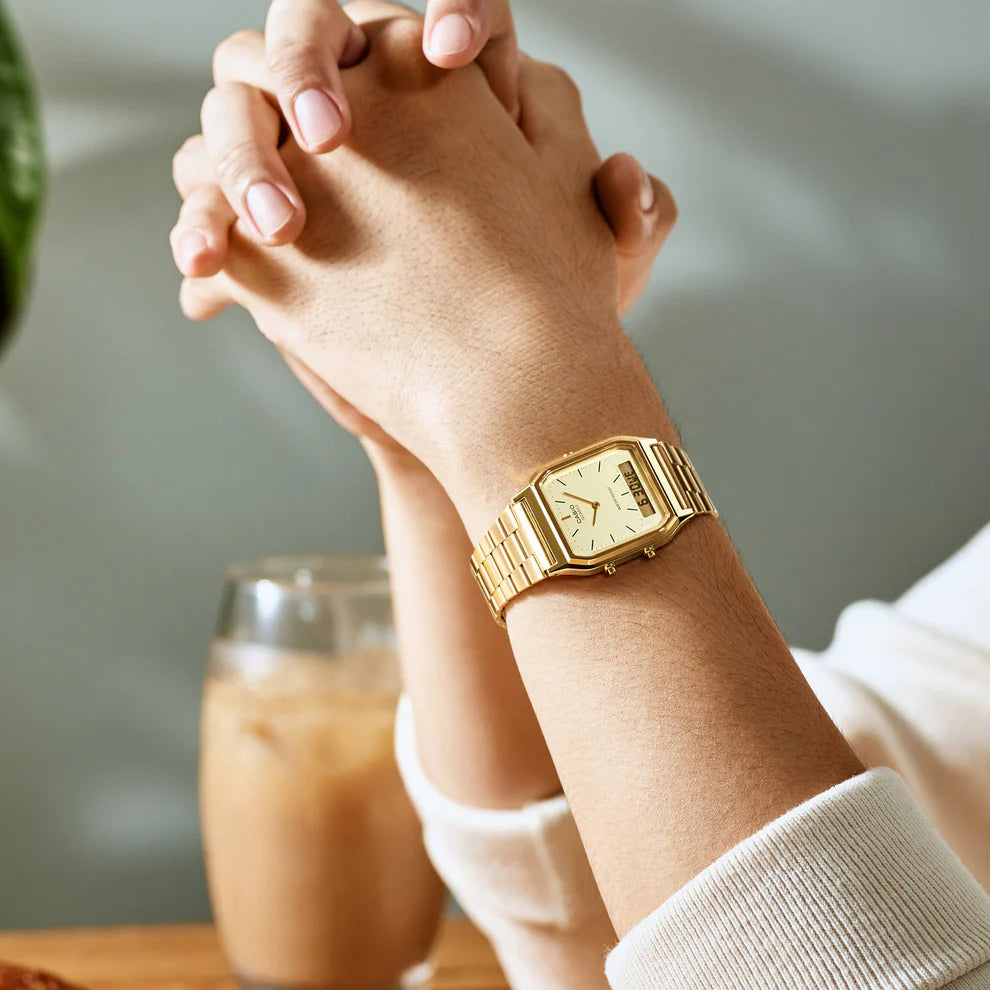 Reloj Casio analógico dorado con brazalete metálico lucido en la muñeca de una persona con las manos entrelazadas.