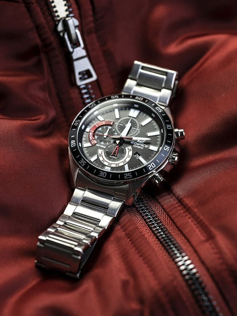 Reloj Casio Edifice de acero con esfera negra y detalles rojos colocado en posición horizontal sobre una chaqueta roja con cremallera.