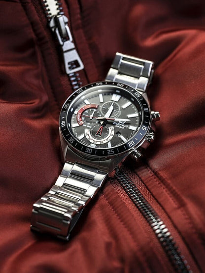 Reloj Casio Edifice de acero con esfera negra y detalles rojos colocado en posición horizontal sobre una chaqueta roja con cremallera.