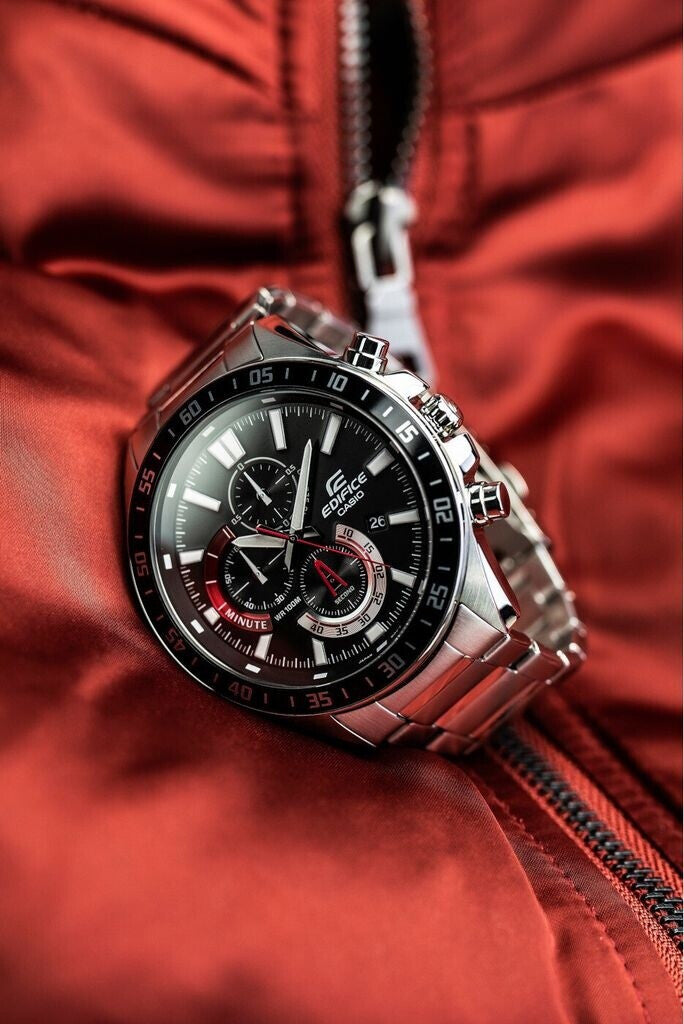 Reloj Casio Edifice de acero con esfera negra y detalles rojos colocado en posición inclinada sobre una chaqueta roja con cremallera.