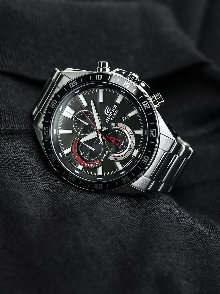 Reloj Casio Edifice de acero con esfera negra y detalles rojos colocado en posición vertical sobre una prenda oscura.