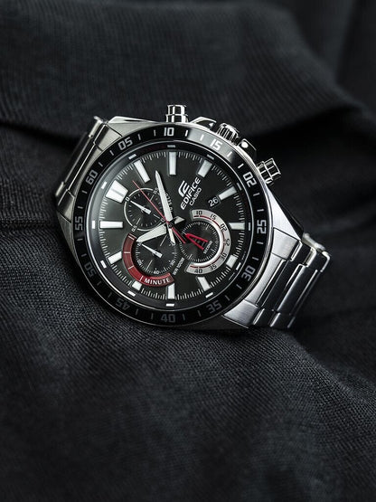 Reloj Casio Edifice de acero con esfera negra y detalles rojos colocado en posición vertical sobre una prenda oscura.
