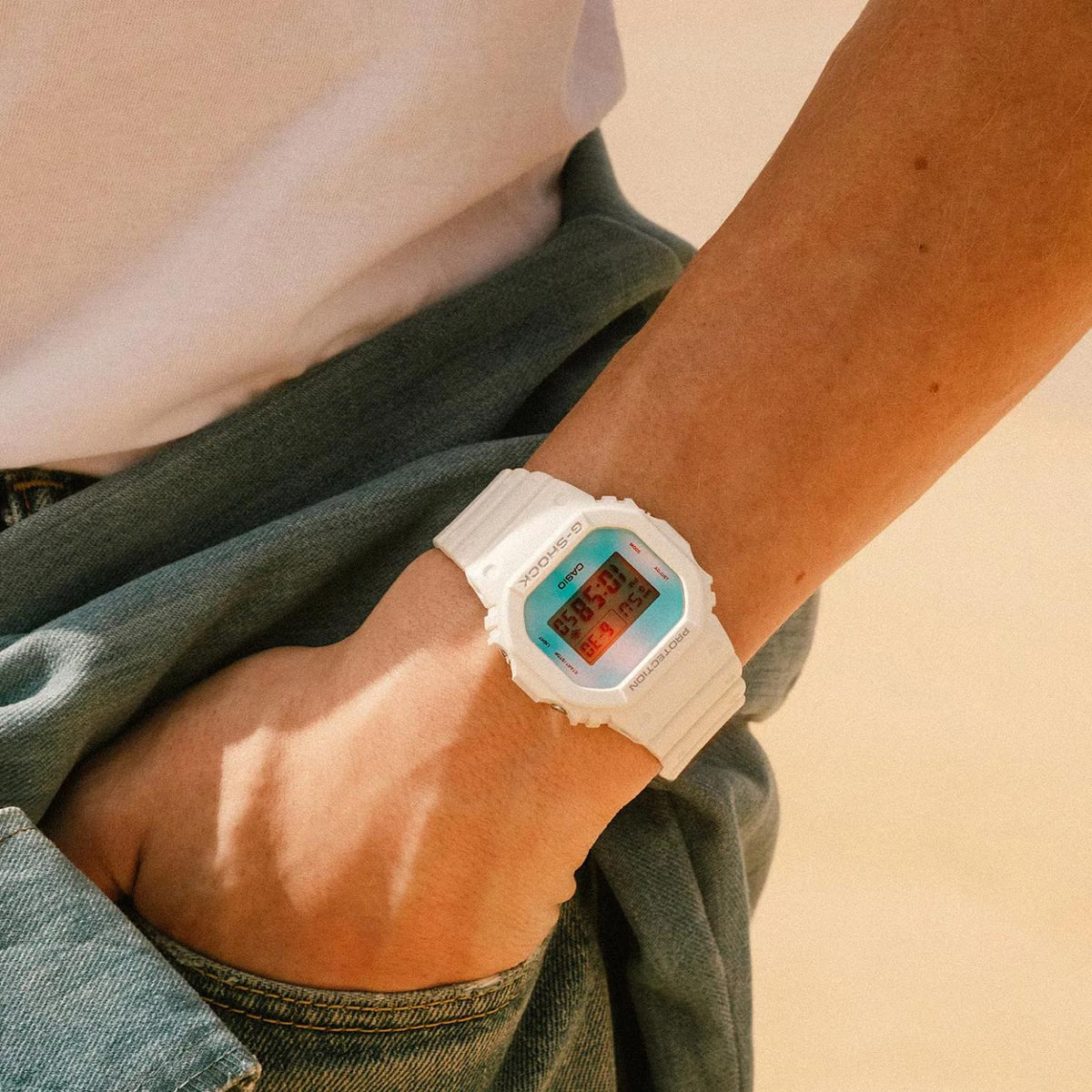 Casio G-Shock DW-5600TL-7 men’s digital watch with a white case and strap, square digital display, and iridescent color-shifting dial worn on the wrist.
