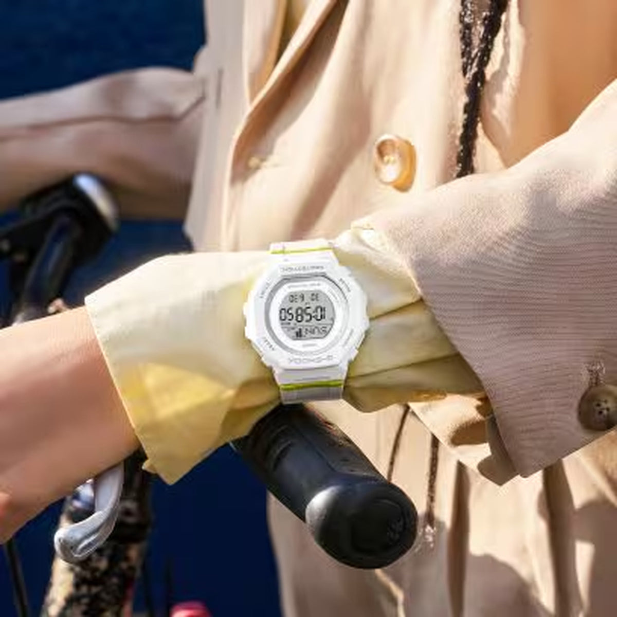 Casio G-Shock G-Squad GMD-B300SC-7 worn on the wrist with digital LCD display, white resin case and strap, gray bezel details, and lime green accents in a casual lifestyle setting.
