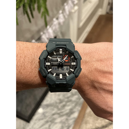 Casio G-Shock GA-010-2A with a black analog-digital dial, silver-tone markers, red accents, and a dark green resin case and strap worn on the wrist.
