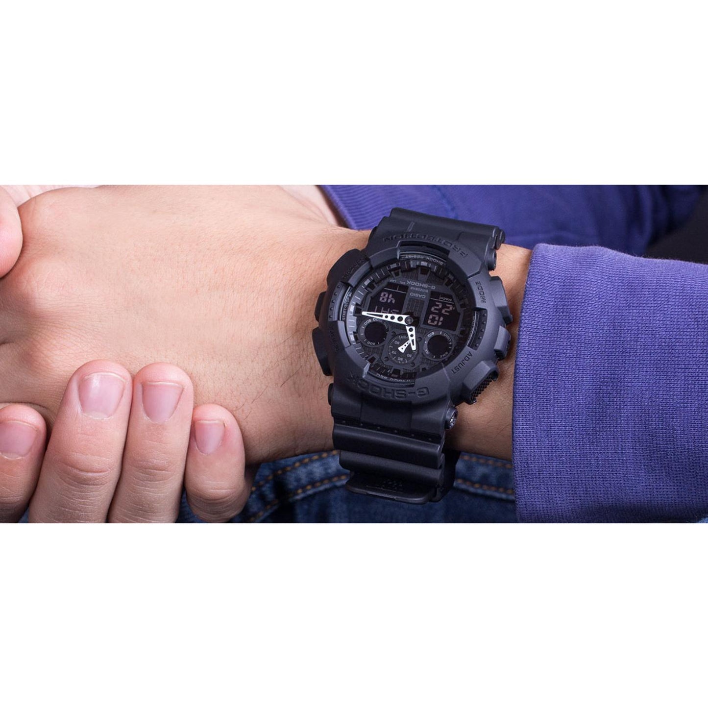 Casio G-Shock GA-100-1A1 worn on the wrist, featuring an all-black analog-digital display, shock-resistant resin case, and black resin strap in a casual everyday setting.