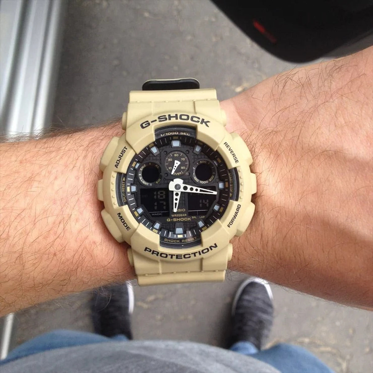 Casio G-Shock GA-100L-8A ana-digi sports watch worn on the wrist, displaying the bold black dial and tan band.
