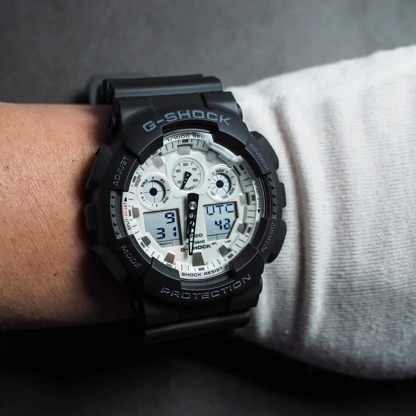 Casio G-Shock GA-100WD-1A worn on the wrist with a white analog-digital dial, black shock-resistant case, and matching black resin band.