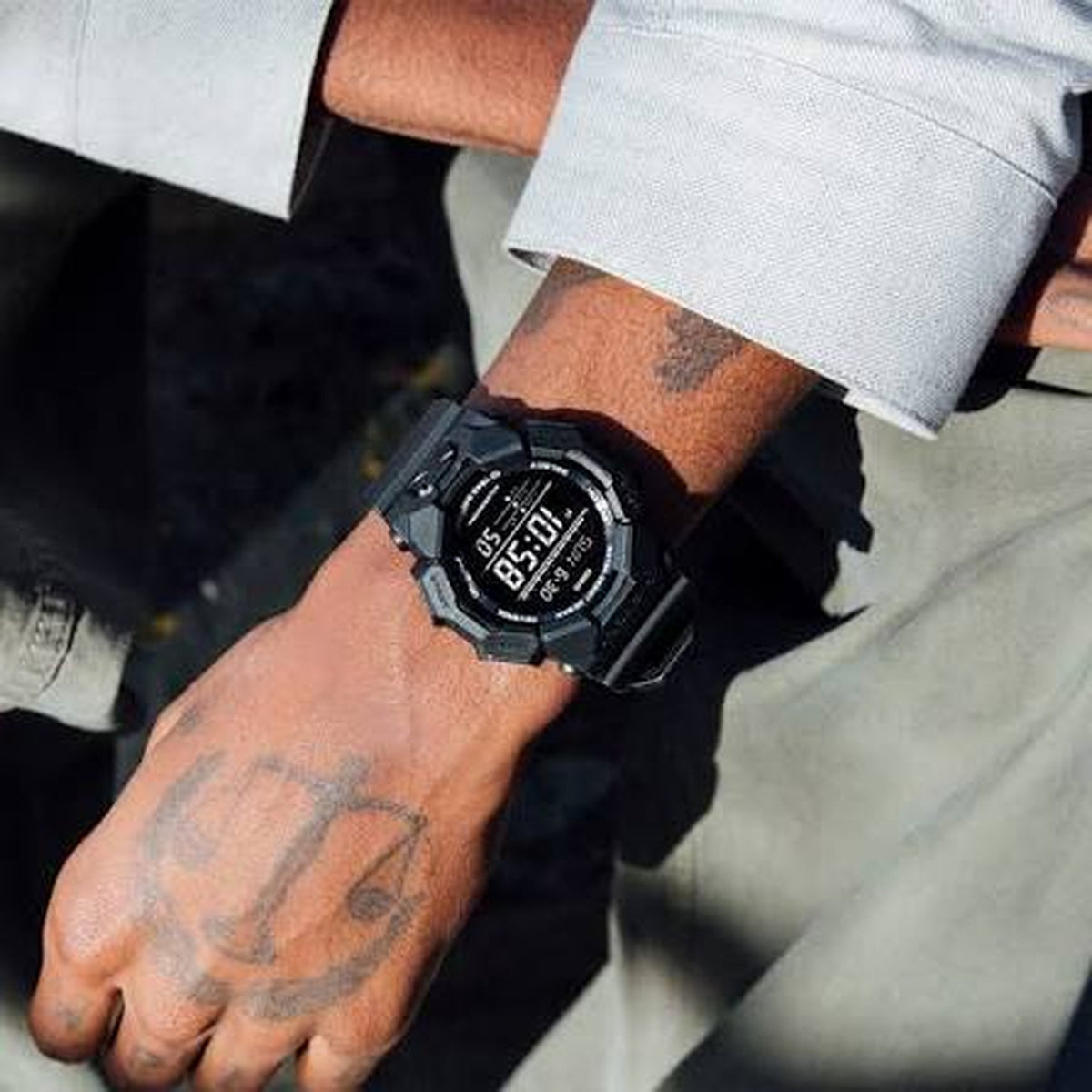 Casio G-Shock GD-010-1DR durable digital sport watch on a wrist with a tattooed hand, showcasing the resilient black resin strap and bezel design.