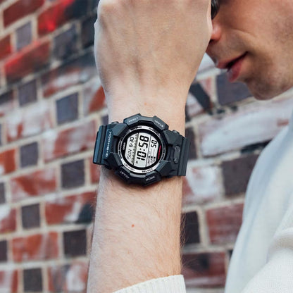 Casio G-Shock GD-010-1DR men's digital sport watch worn on the wrist against a brick wall backdrop, highlighting the robust black resin case and clear digital display.