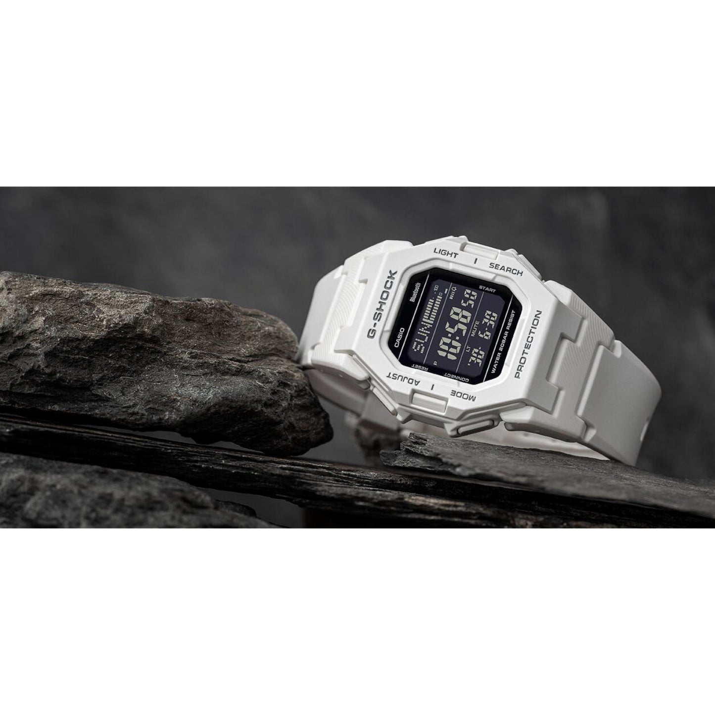 Casio G-Shock GD-B500-7 digital sport watch displayed on rocks, featuring a white resin case and strap, black digital display, and rugged shock-resistant design.