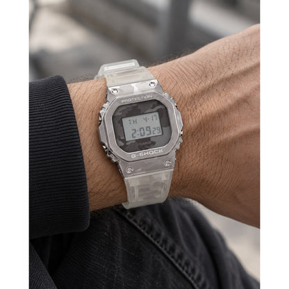 Casio G-Shock GM-5600SCM-1 digital men's watch worn on a wrist, featuring a metallic bezel and translucent camouflage resin strap.
