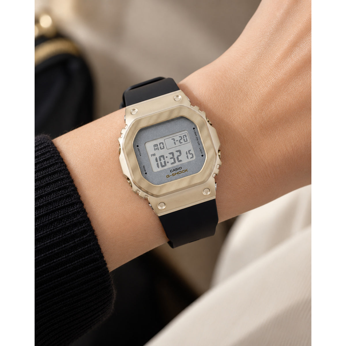Casio G-Shock GM-S5600BC-1 women’s digital watch with a gold-tone square bezel, light digital display, gray dial surround, and black strap worn on the wrist.