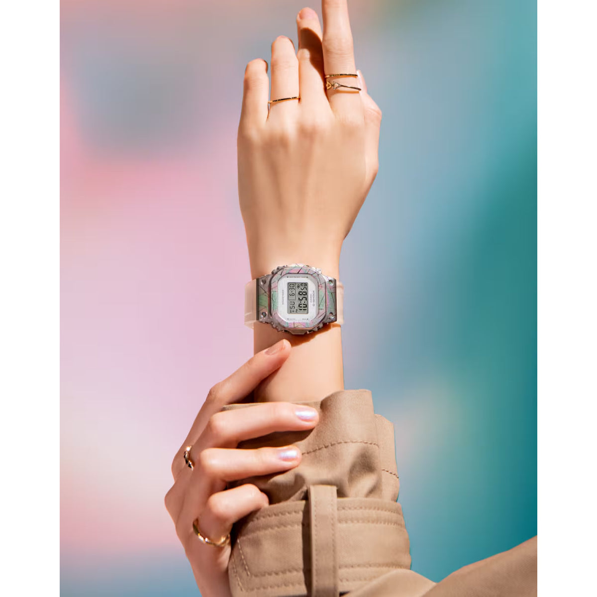 Casio G-Shock GM-S5640GEM-7DR women’s digital watch with an iridescent rainbow-tone bezel, square digital display, and translucent white strap worn on the wrist.