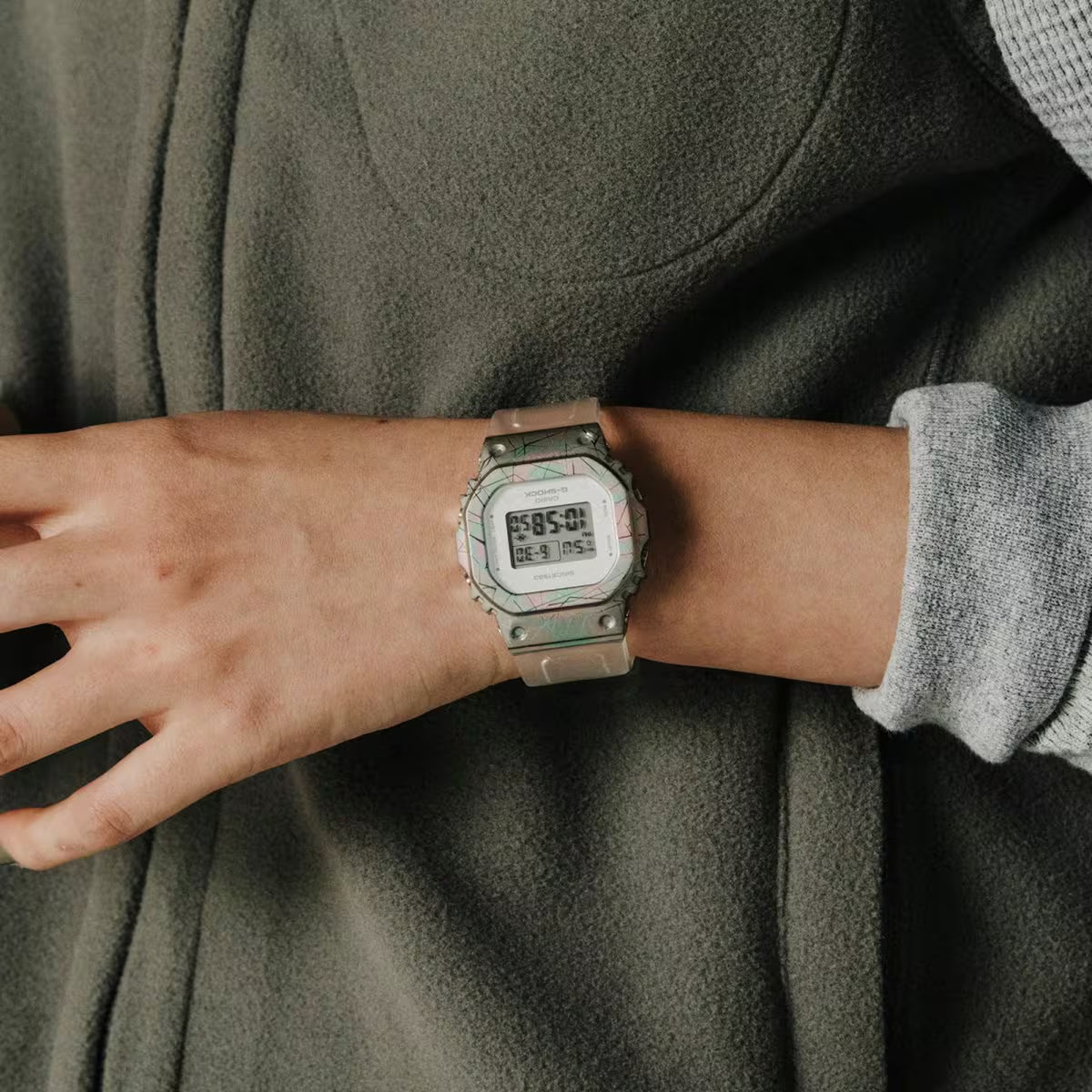 Casio G-Shock GM-S5640GEM-7DR women’s digital watch with an iridescent rainbow-tone bezel, square digital display, and translucent white strap worn on the wrist.